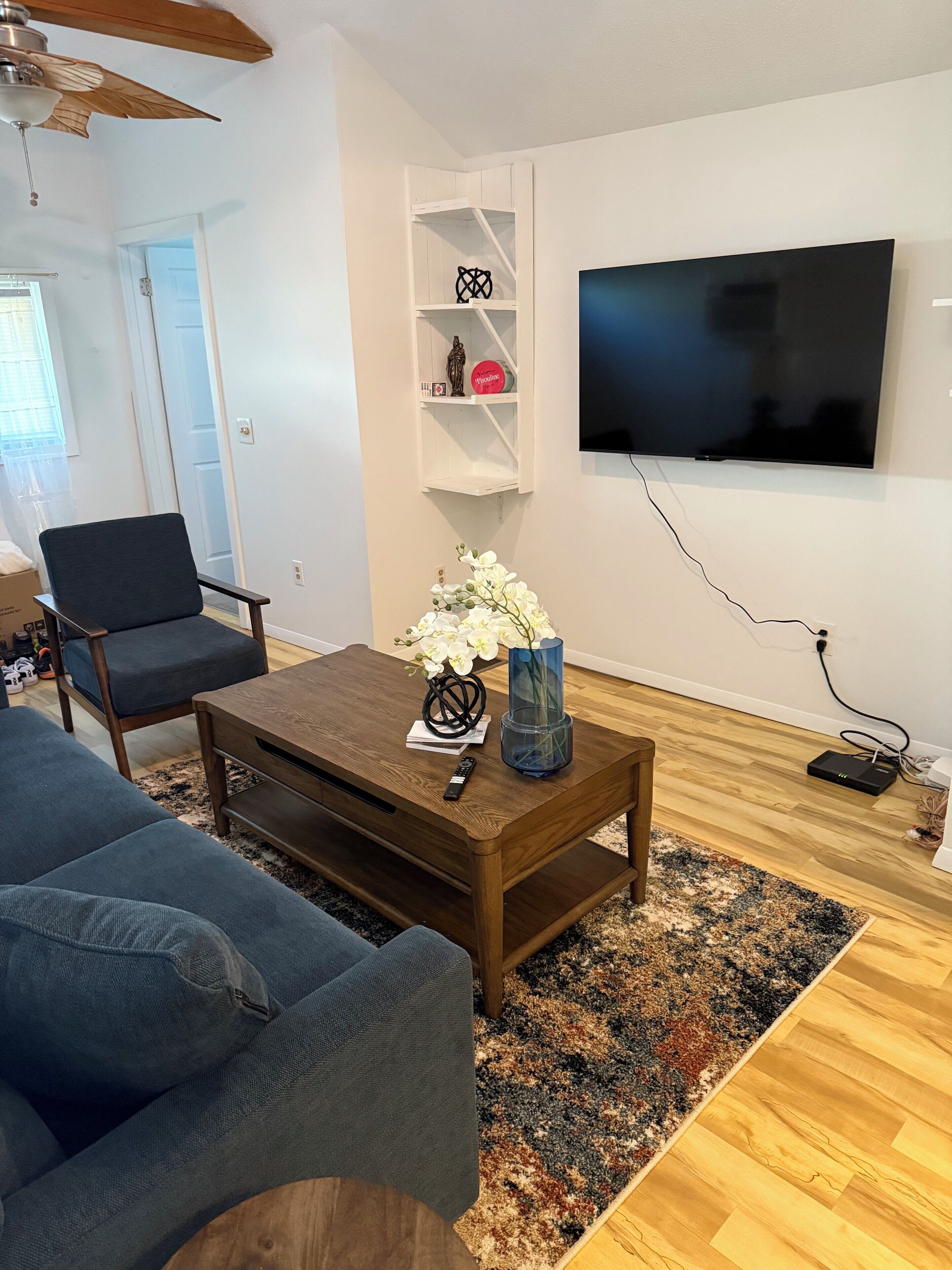 A living room with a sofa, a coffee table with a vase and remote, a TV on the wall, and a wooden floor.