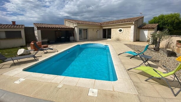 Una piscina amb gandules, un porxo cobert i un edifici amb teulada enrajolada.