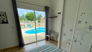 Un dormitori amb un llit, vista a una piscina i una porta corredissa de vidre.