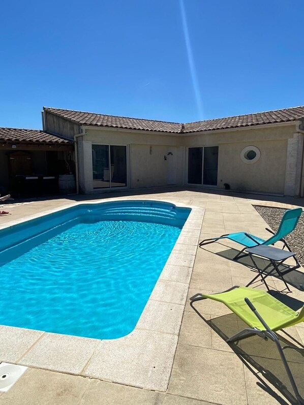 A rectangular swimming pool with clear blue water, surrounded by a tiled patio with outdoor furniture. - House with swimming pool near Vaison-la-Romaine (Séguret)