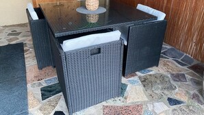 Taula de dinar de vimet negre amb una jardiniera teixida a sobre, envoltada de cadires a joc.
