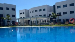 A swimming pool with a covered seating area, surrounded by modern buildings. - Newbuild apartment Estepona pool - beach - gym (Estepona)