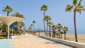 A paved walkway lined with palm trees and a beach in the background. - Newbuild apartment Estepona pool - beach - gym (Estepona)