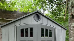 A gray shed with a peaked roof, two doors, and a small window on the upper door. - The Best of Both Worlds – 3 bedroom house with Lake Access Without the Crowds (Mears)
