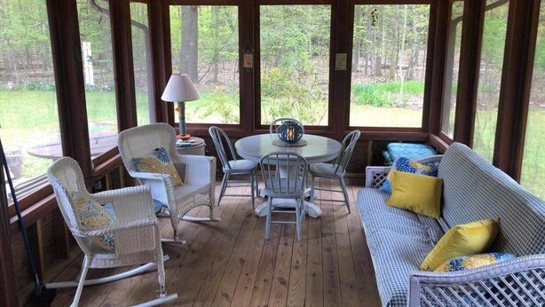 A covered outdoor seating area with wicker furniture, a round table, and string lights. - The Best of Both Worlds – 3 bedroom house with Lake Access Without the Crowds (Mears)