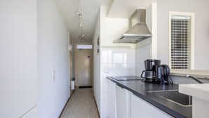 A modern kitchen with white cabinets, a stainless steel sink, and a coffee maker. - Ameland - Quiet apartment near the beach with terrace and pool access (Hollum)