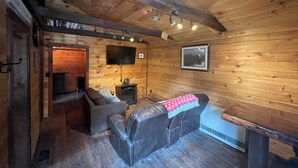 Un acogedor interior de cabaña con techo de madera, chimenea, sofá y televisión.