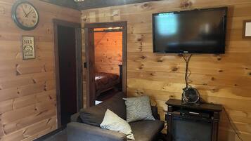 Un salon chaleureux avec un canapé, un téléviseur à écran plat fixé au mur et un plafond en bois.