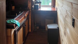 Cocina estrecha con paredes de madera, una ventana, un lavamanos y un cubo de basura.