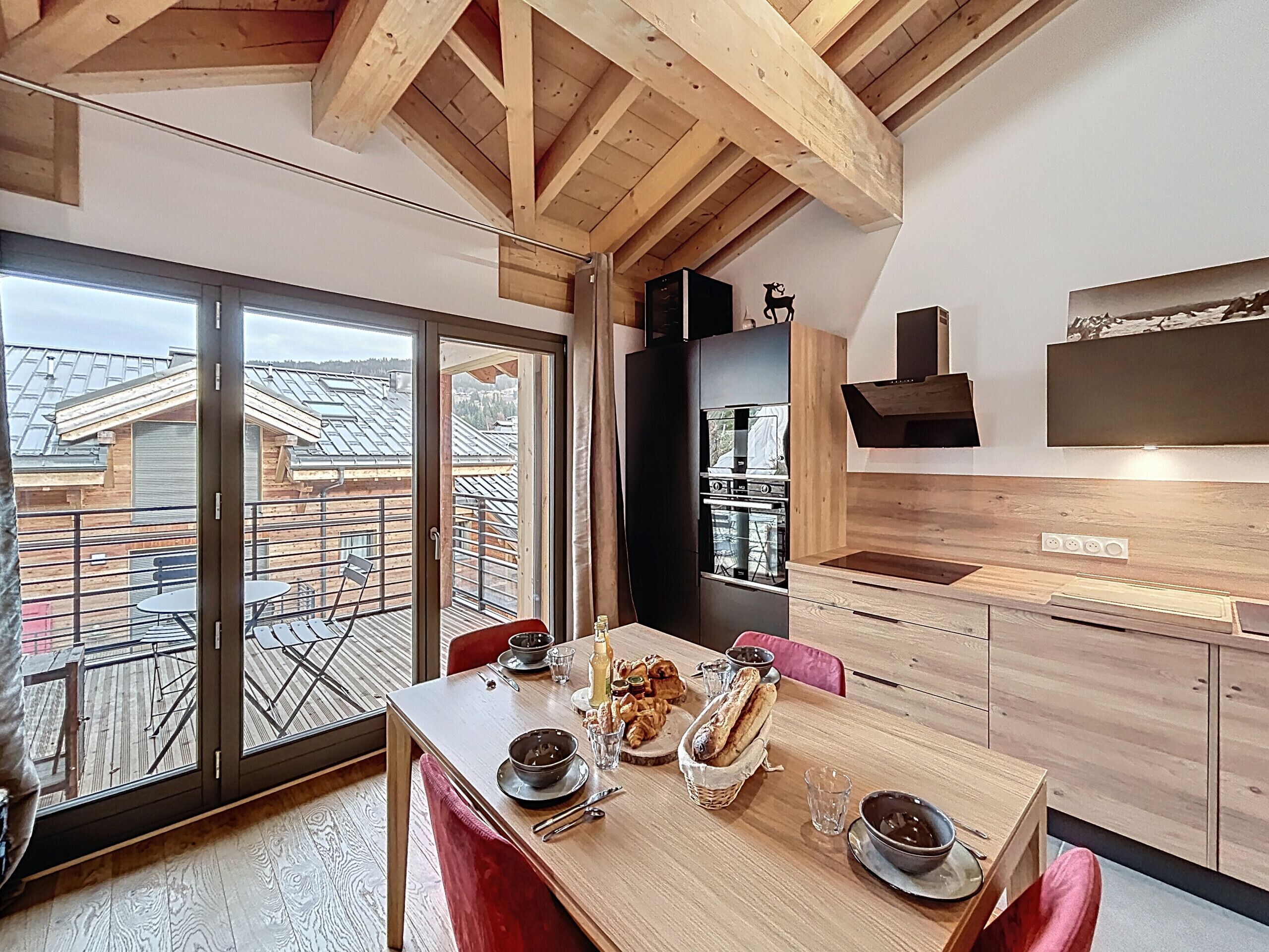 Een moderne keuken met houten kastjes, een inbouwoven en een eethoek met een tafel gedekt voor twee personen.