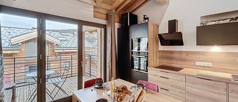 Een moderne keuken met houten kastjes, een inbouwoven en een eethoek met een tafel gedekt voor twee personen.