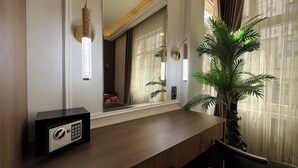 Ein Hotelzimmer mit einem Holztischchen, einem Safe, einem großen Spiegel und einer Zimmerpflanze.