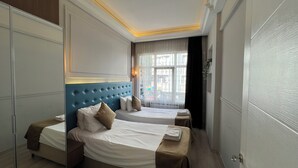 Ein Hotelzimmer mit zwei Betten, einem großen Fenster mit transparenten Vorhängen und einer Wandleuchte.