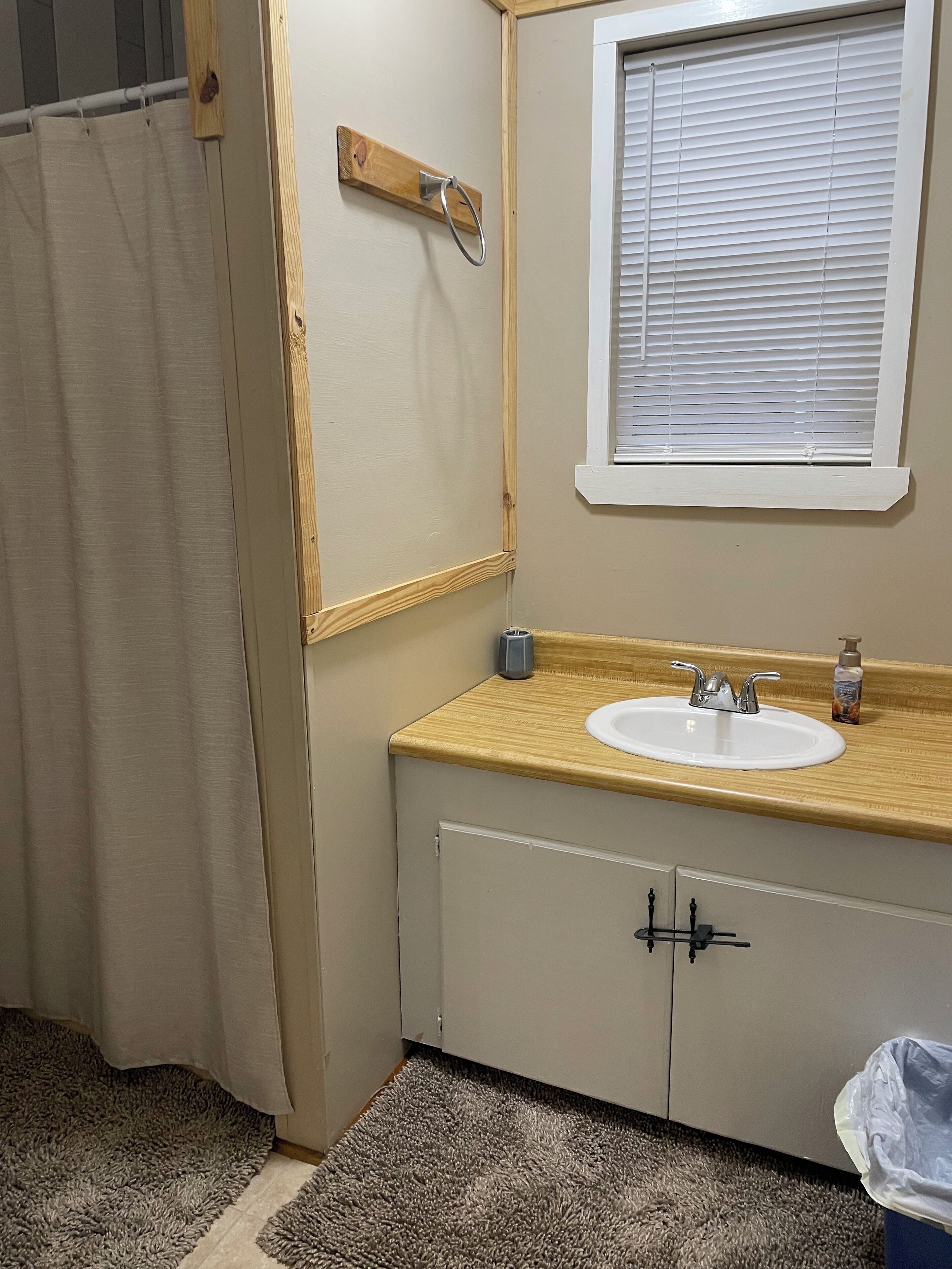Ein Badezimmer mit einem beigen Waschbecken, einem Holzwaschtisch und einem Fenster mit Jalousien.