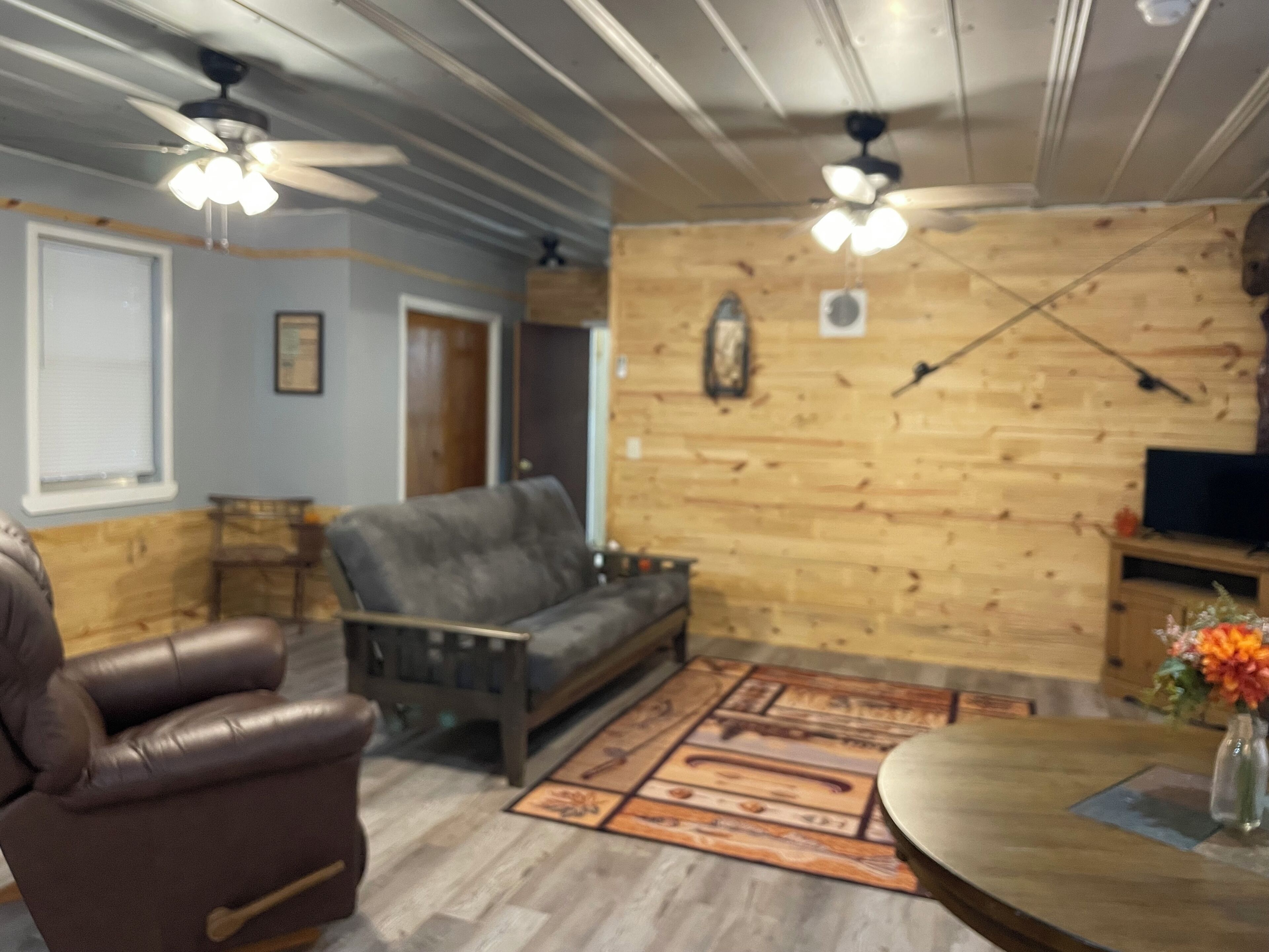 Un salon avec un canapé, un fauteuil, un plancher en bois, un ventilateur de plafond et un téléviseur.