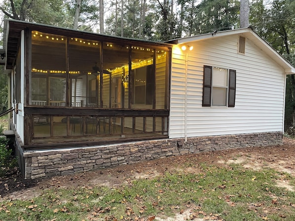 A cabin with a large screened porch, stone foundation, and string lights.