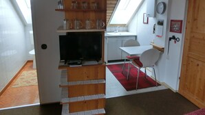Eine kompakte Küche mit integriertem Fernseher, einer kleinen Essecke und einem roten Teppich.