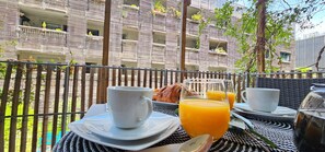 Et udendørs spiseområde med et bord dækket til morgenmad, inklusive croissanter og appelsinjuice.