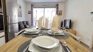A dining area with a wooden table set for four, a refrigerator, a TV, and a balcony with a view. - Cosy Apartment In A Green Setting -Nice (Nice)