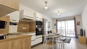 A modern kitchen with wooden cabinets, a dining area with a table and chairs, and a balcony with a view. - Cosy Apartment In A Green Setting -Nice (Nice)