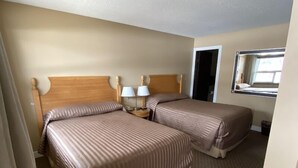 A hotel room with two beds, a small bedside table with lamps, and a mirror on the wall. - Twin Creeks Motel (Lumby)