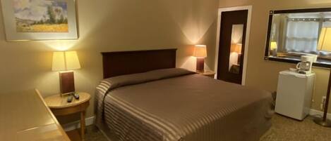 A hotel room with a bed, bedside lamps, a desk, a small table, a mirror, and a picture on the wall.
