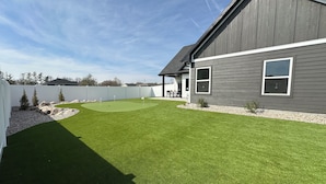 A residential property with a well-maintained lawn, a white fence, and a house with a dark exterior.