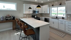 A modern kitchen with a central island, pendant lighting, and a view of the outdoors.