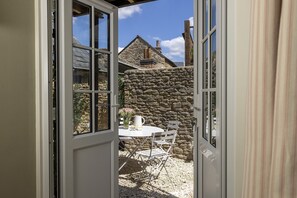 An open door leading to a stone wall and a small patio with a table and chairs.