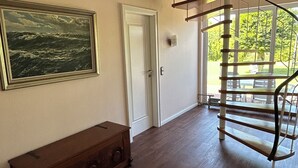 Une pièce spacieuse dotée d’un parquet, d’un banc en bois, d’un grand tableau encadré, d’une porte blanche et d’un escalier en colimaçon menant à un espace extérieur.