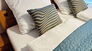 Un lit avec des oreillers blancs et à rayures, une couverture bleue matelassée et une table de chevet en bois.