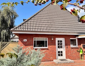 A red brick house with a tiled roof, a white door, and a window with a view of the interior.