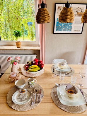 A dining table set with plates, cutlery, glasses, and a bowl of fruit.