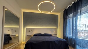 Een moderne slaapkamer met een groot bed, nachtkastjes, een spiegel en een ronde lamp.