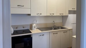 Een moderne keuken met witte kasten, een inbouwoven, waterkoker, spoelbak en een koelkast.