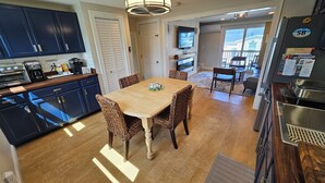 A modern kitchen with dark cabinets, a wooden dining table, wicker chairs, and a ceiling light fixture.