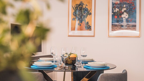 A dining table set with plates, glasses, and a fruit bowl, with two framed paintings on the wall. - MT apartment - Elegant apartment and well connected (Roma)