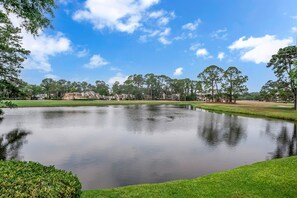 A serene lake with a clear sky, surrounded by lush greenery and residential buildings. - 191 Twin Oaks at The Sea Pines Resort (Hilton Head Island)