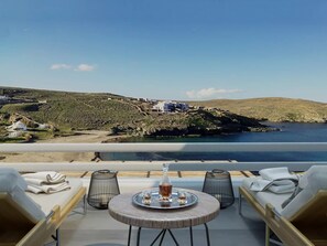 A terrace with a table set for two, overlooking a coastal landscape with buildings and hills. - Mykonos Marina's Maisonette Merchia (Mykonos)