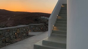 Een trap die leidt naar een wit gebouw met uitzicht op een glooiend landschap en een zonsondergang.