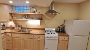 Une cuisine avec des meubles de rangement en bois, un évier en acier inoxydable, une cuisinière à gaz et un réfrigérateur blanc.