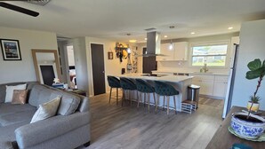 A modern living room with a grey sofa, a wooden coffee table, and a kitchen area with a bar stool set. - Charming 2-bedroom house in New Port Richey with WiFi, AC. Close to downtown (New Port Richey)