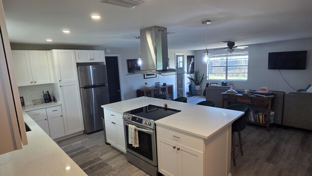 A modern kitchen with white cabinetry, a stainless steel refrigerator, a built-in oven, and a central island. - Charming 2-bedroom house in New Port Richey with WiFi, AC. Close to downtown (New Port Richey)