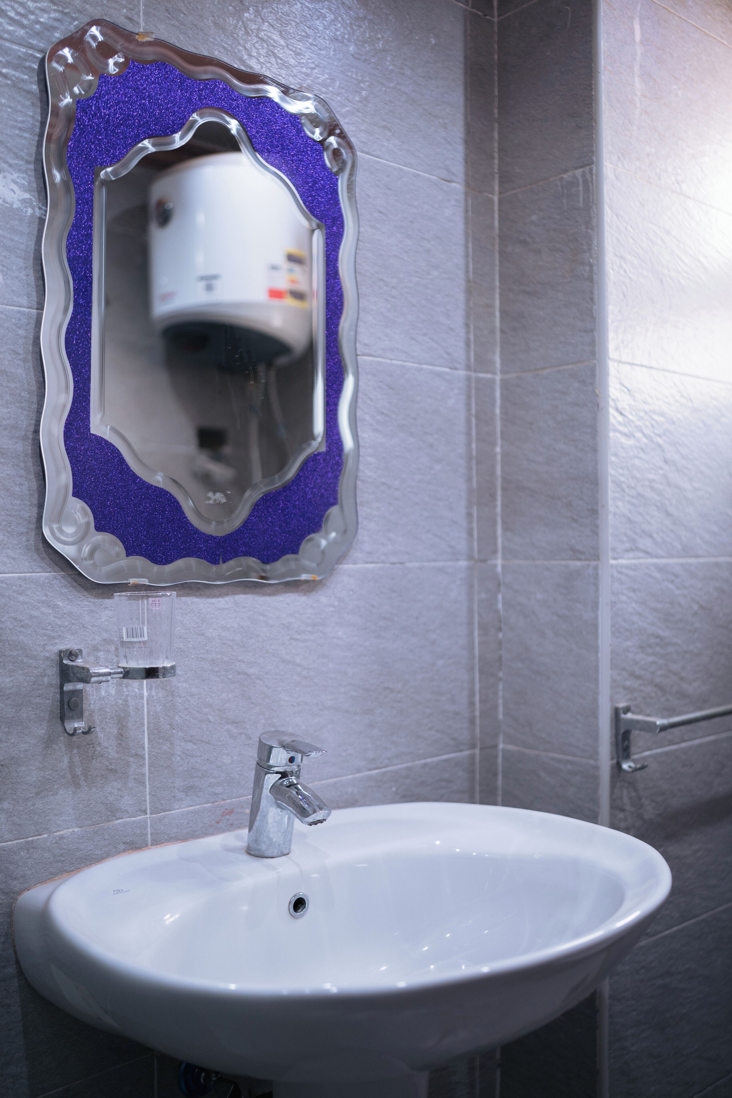 Un baño con un lavabo blanco, un espejo con marco decorativo y un secador de manos.