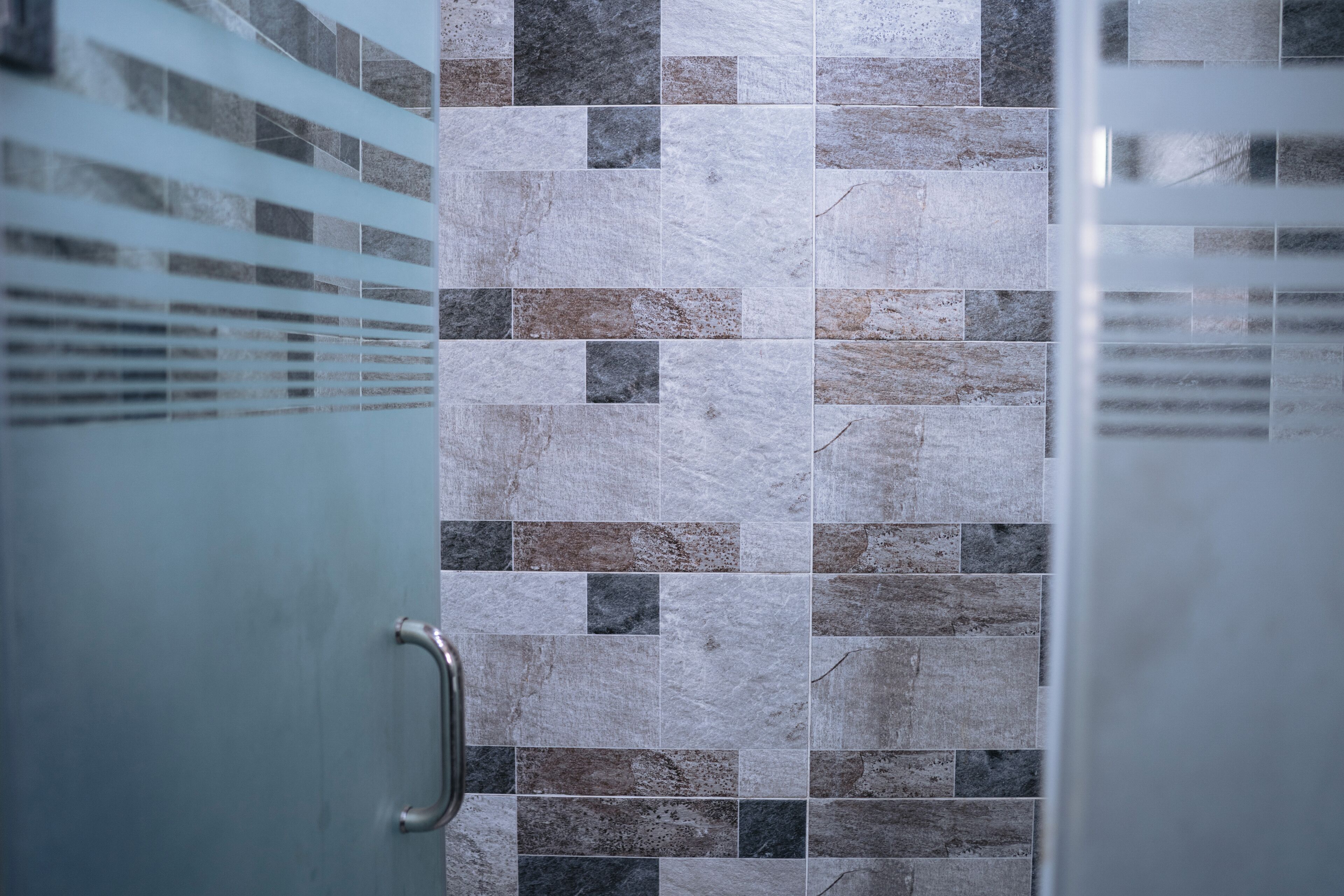 A bathroom with a tiled wall and a glass door with a metal handle.
