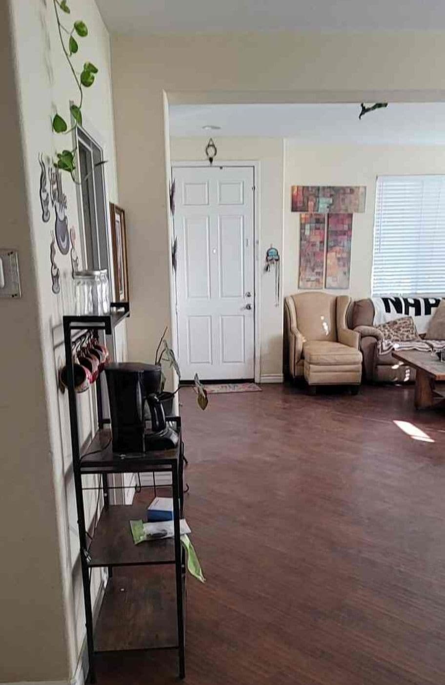 A living room with a wooden floor, a sofa, a coffee table, and a door with a coat hanging on the wall.