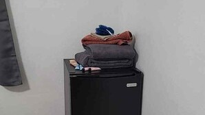 Een kleine, zwarte koelkast met een stapje opgevouwen kleding en een boek erboven.