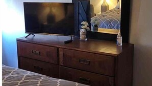 Een hotelkamer met een bed, een kaptafel met spiegel, een televisie en een nachtkastje met lamp en bloemen.