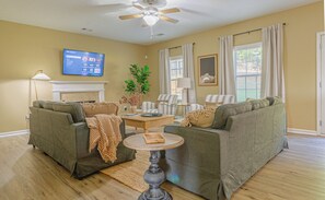 Ein Wohnzimmer mit zwei Sofas, einem Couchtisch, einem an der Wand befestigten Fernseher und einem Deckenventilator.