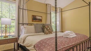 A four-poster bed with a floral bedspread, a bedside table with a lamp, and a window with curtains. - Spacious Gem Near Fort Moore  (Columbus)